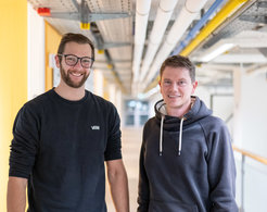 Tim Schulte and Prof. Tobias Ritter stand side by side in the hallway of the laboratory building at the Max-Planck-Institut für Kohlenforschung in Prof. Ritter's department.