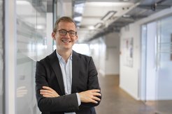 Mann in dunklem Anzug und hellblauem Hemd im modernen Büroflur.